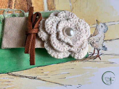 White crocheted flower with a brown leather strap on a textured surface hair clip by zerofossil